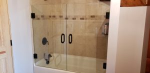 a glass shower and tub enclosure with bronze hardware